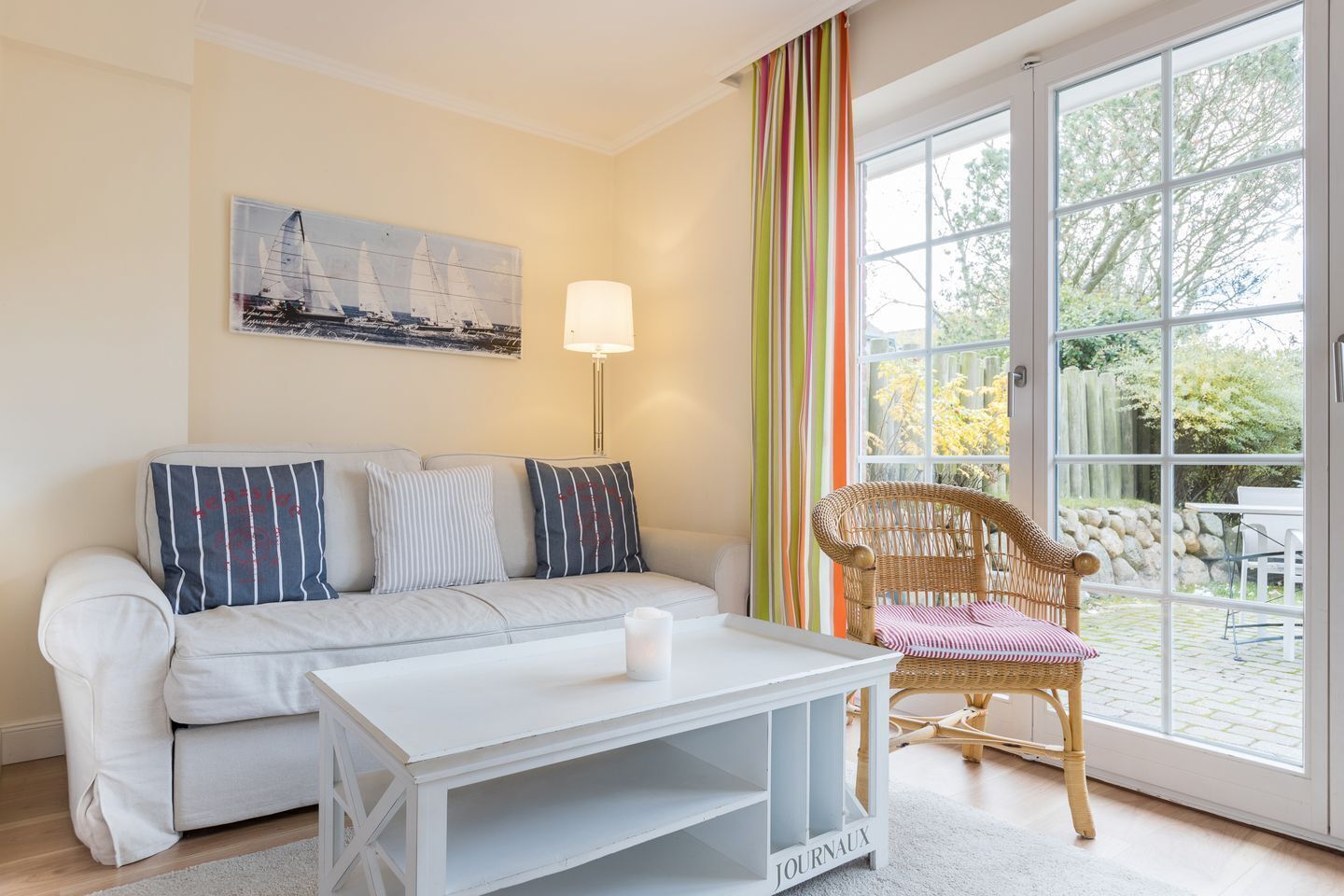 Ein modernes Wohnzimmer mit Sofa, Couchtisch, Korbstuhl, Lampe und einem großen Fenster mit Blick ins Freie.