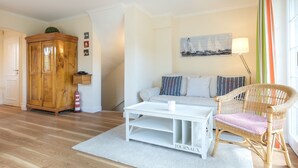 A cozy living room with a white sofa, a wicker chair, a white coffee table, and a wooden cabinet.