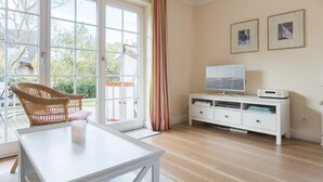 A room with a large sliding glass door leading to a balcony, a white TV stand with a flat-screen TV, and a wicker chair.