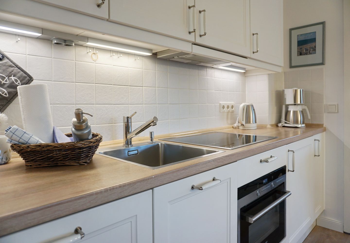 A modern kitchen with white cabinets, a stainless steel sink, a built-in oven, and a coffee maker.