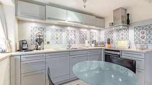 A modern kitchen with light grey cabinets, a glass table, and patterned backsplash tiles.