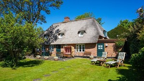 A thatched-roof house with a brick extension, a lawn, and outdoor seating.