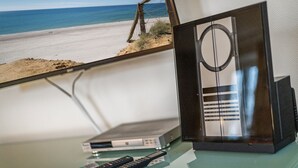 A room with a beach view, a television, and a DVD player on a glass table.