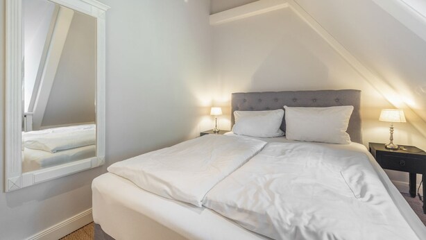 Une chambre à coucher avec un grand lit, deux tables de chevet et un miroir.