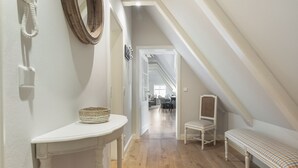 Un couloir avec une console blanche, un panier en osier, un banc et un miroir accroché au mur.