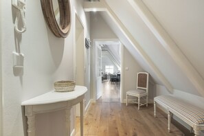 Un couloir avec une console blanche, un panier en osier, un banc et un miroir accroché au mur.