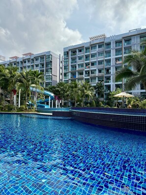 A swimming pool with a tiled edge, a water slide, and a building with balconies in the background. - Dusit Grand Park by PSR (Pattaya)