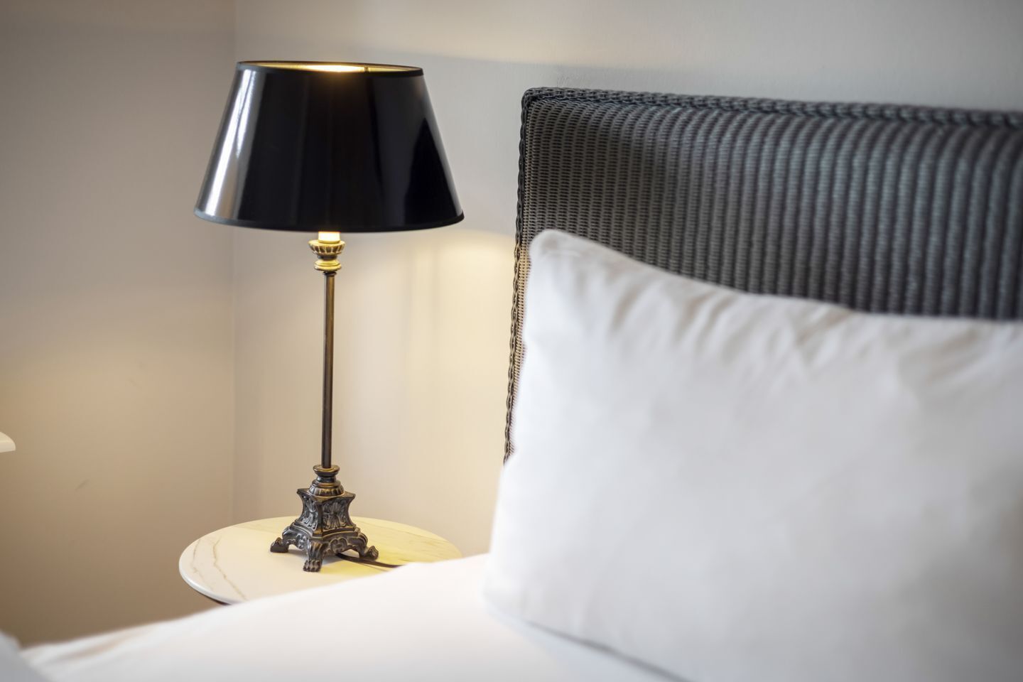 A bed with a white pillow and a black lamp with a gold base on a white nightstand.