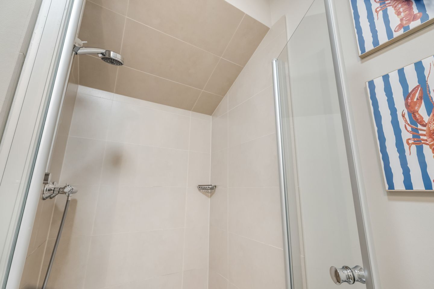 A glass-enclosed shower stall with beige tiles, a handheld showerhead, and a wall-mounted faucet.