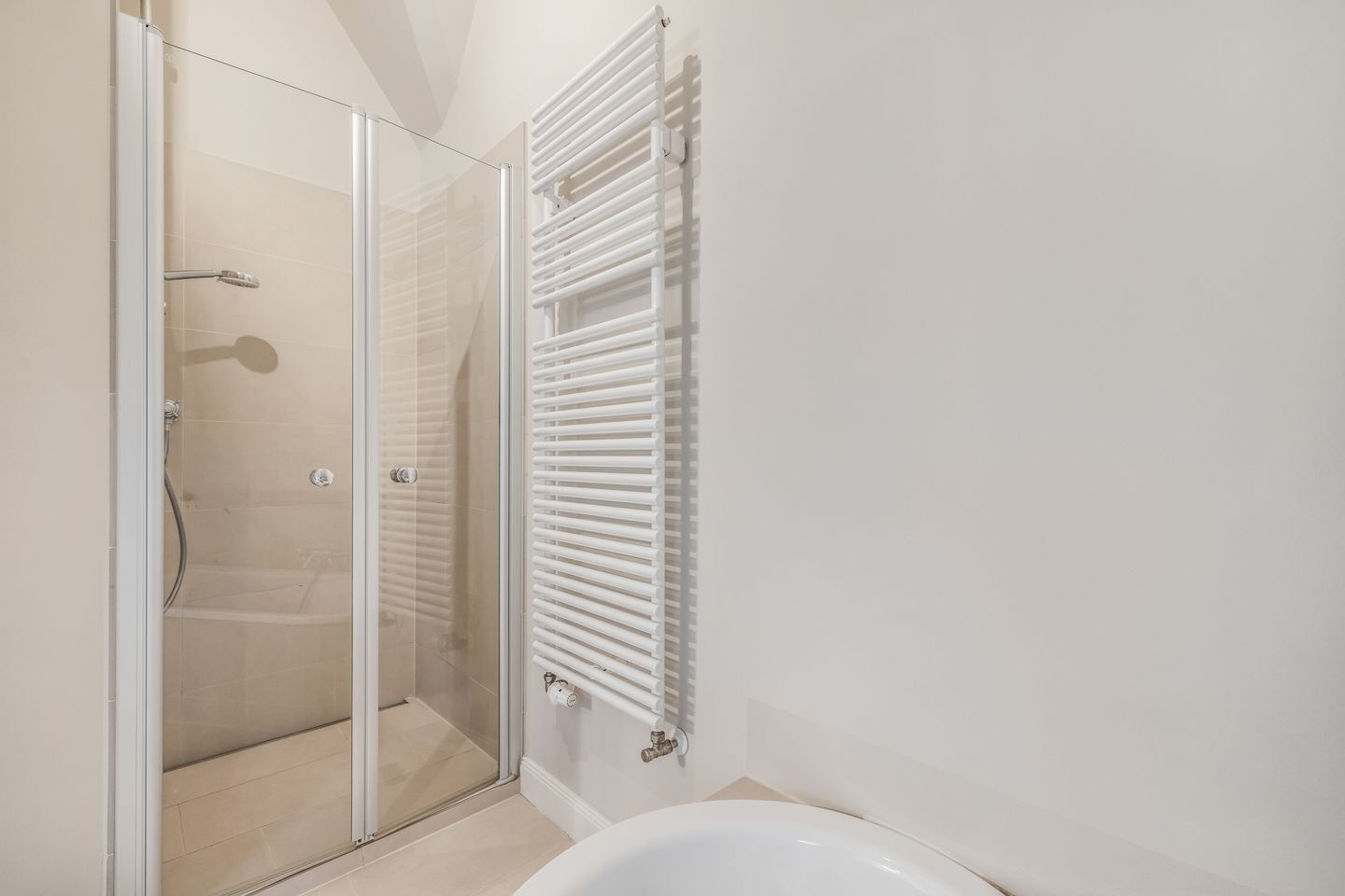 Uma casa de banho com cabine de duche em vidro, uma banheira branca e um radiador toalheiro branco.
