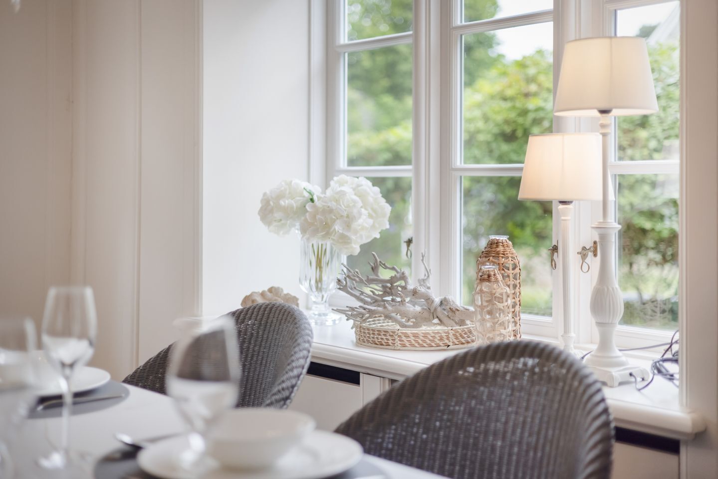 A dining table set with white plates, glasses, and a vase of white flowers.