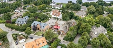 Eine Vogelperspektive auf ein Küstendorf mit traditionellen Häusern, einem zentralen Gebäude mit rotem Dach und einem Gewässer im Hintergrund.