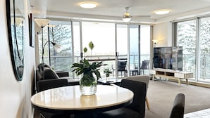 A modern interior with a round table, dark chairs, a large window, and a television. - Beach View 2 Bedrooms Apartment  (Surfers Paradise)