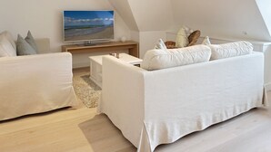 Camera da loft moderna con una grande finestra, una TV a schermo piatto, un divano bianco e un tavolino.