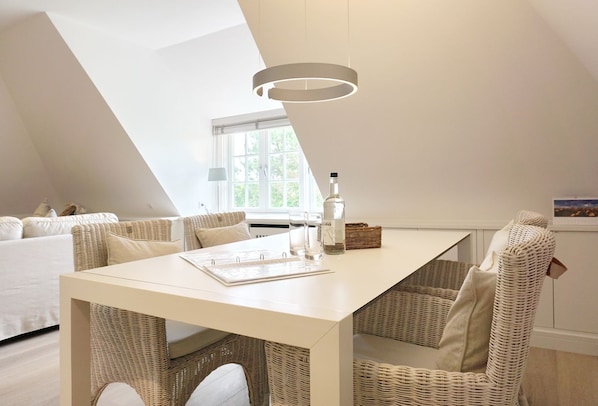 Une chambre à coucher de style loft moderne, avec un plafond en pente, une table à manger blanche, des meubles en osier et une grande fenêtre.