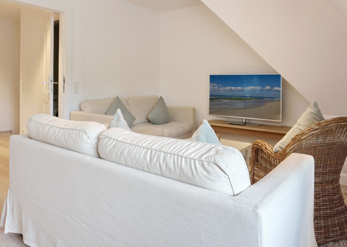 Una sala moderna con un sofá blanco, un televisor y una silla de mimbre.