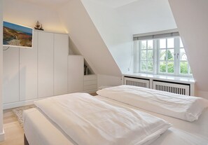 Une chambre avec un plafond en pente, un lit, une fenêtre et une armoire blanche.