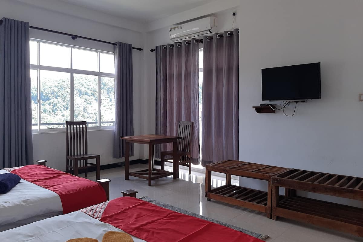 A hotel room with two beds, a TV, a table, and a chair.