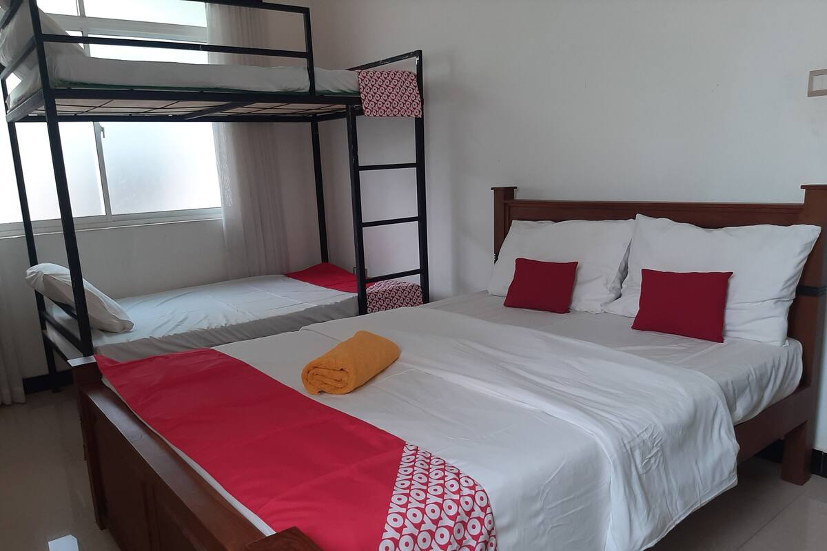 A hotel room with a bunk bed, a single bed, and a wooden headboard.