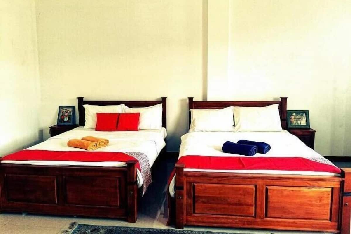 Two wooden beds with red and white bedding, a small nightstand with a picture frame, and a plain wall.