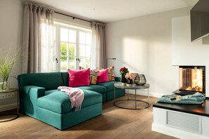 A modern living room with a teal sofa, a round coffee table, and a fireplace. - Calm Island 1 - Ein Wahrgewordener Urlaubstraum Unter Reet (Sylt)
