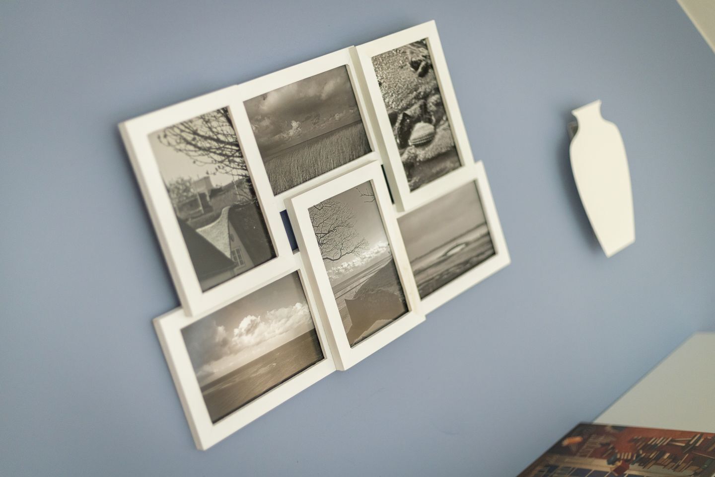 A wall with a collage of black and white photographs and a white vase.
