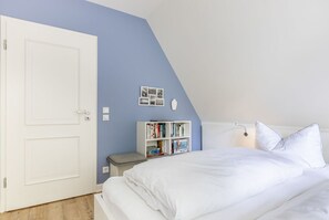 Un dormitorio con una cama blanca, una estantería, una puerta blanca y una pared azul claro.