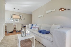 A modern living room with a white sofa, a coffee table, and a dining area with chairs and a table.