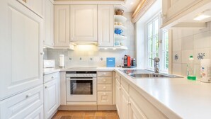 A kitchen with white cabinets, a built-in oven, a sink, and a window providing natural light. - Tüchter - Tüchter - Tolle Ferienwohnung in Südostlage Wenige Gehminuten vom Wattenmeer (Sylt)