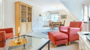 A spacious living room with a glass coffee table, a red sofa, and a wooden cabinet. - Tüchter - Tüchter - Tolle Ferienwohnung in Südostlage Wenige Gehminuten vom Wattenmeer (Sylt)
