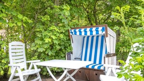 A garden seating area with a striped blue and white chair, a white table, and a white chair. - Tüchter - Tüchter - Tolle Ferienwohnung in Südostlage Wenige Gehminuten vom Wattenmeer (Sylt)