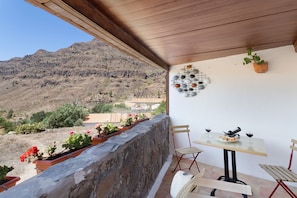 Un balcon avec un mur en pierre, des plantes en pot, une table avec des chaises et une vue sur un paysage montagneux.