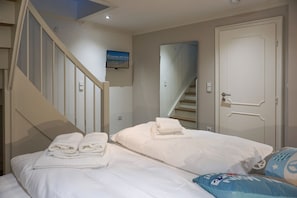 Un dormitorio con cama, televisión, escalera y puerta.