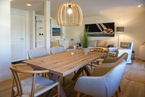 Un comedor moderno con una mesa de madera, sillas acolchadas, una lámpara colgante y un sofá al fondo.
