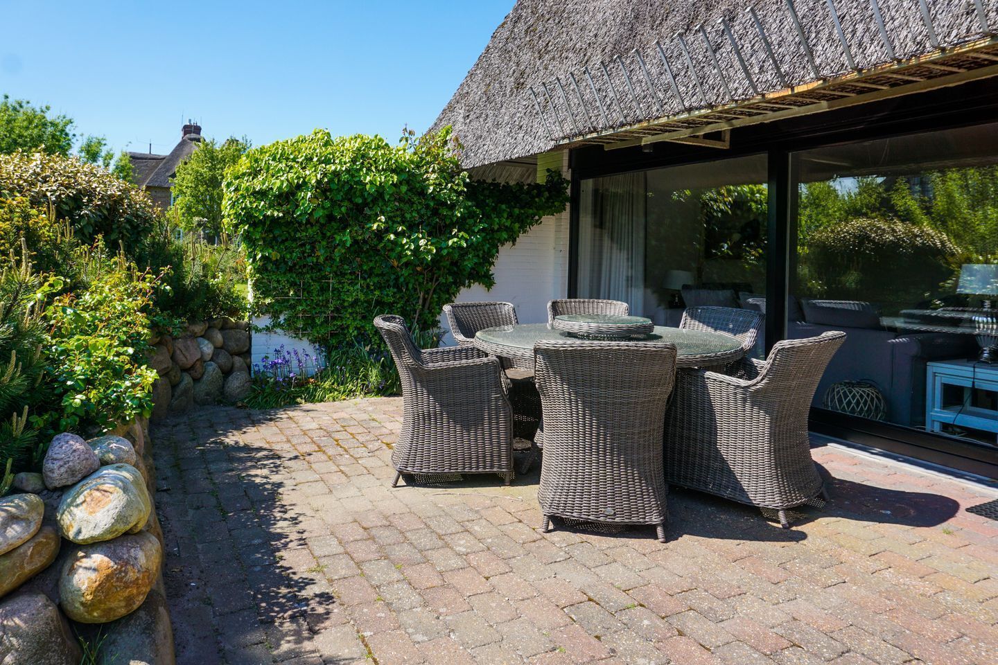 Een terras met rieten meubels, een rieten dak en een stenen muur.
