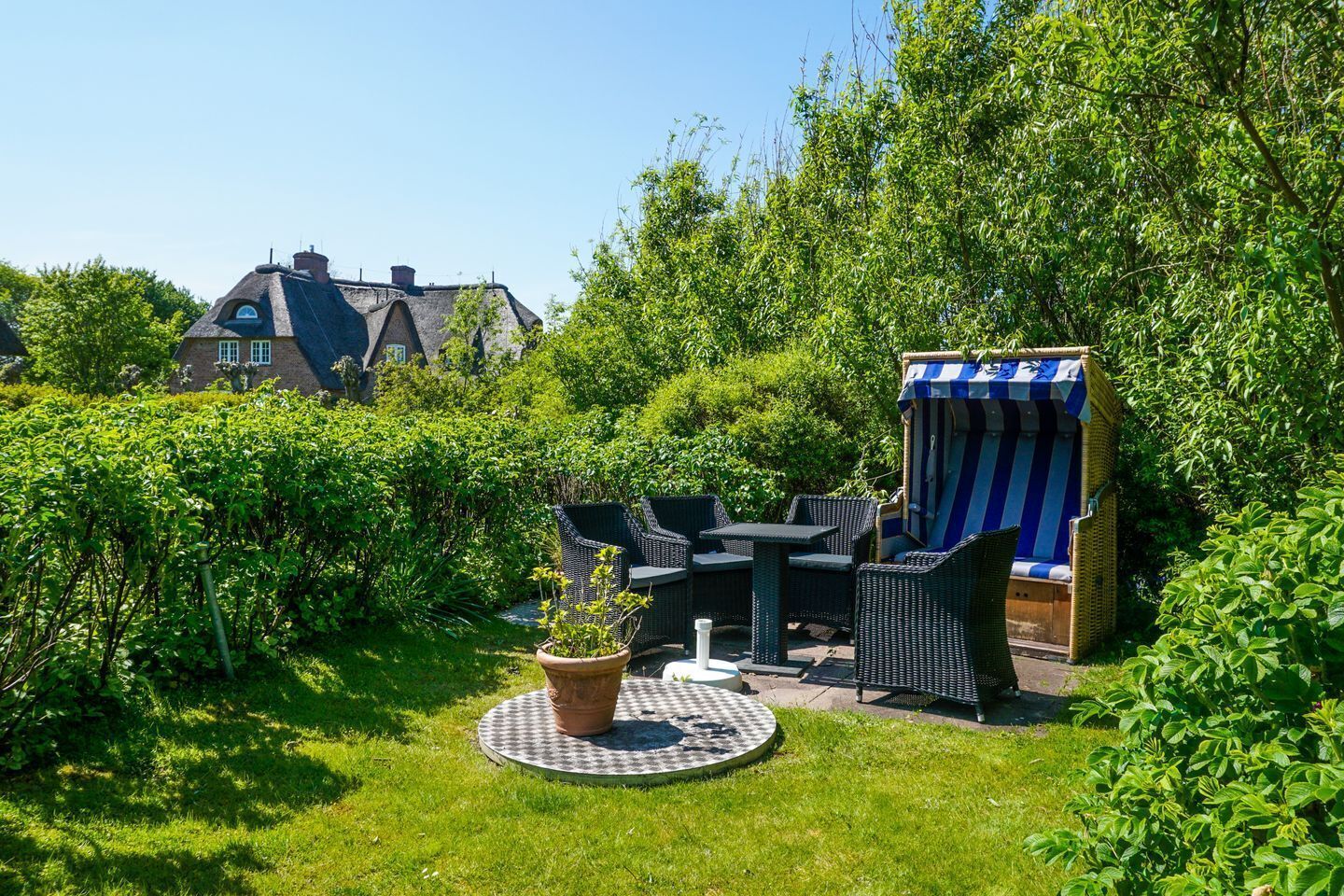 A garden with a table and chairs, a striped awning, and a house in the background.