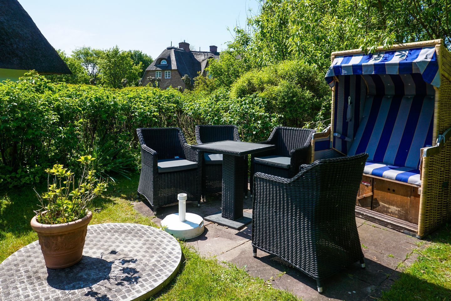 Une terrasse extérieure avec des meubles en osier, une table ronde et un auvent à rayures.