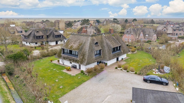 A traditional thatched-roof house with a gravel driveway, surrounded by a grassy lawn and other similar houses in a rural setting. - Uaster Reeg III - Studio - Sehr Gepflegte und Geschmackvoll Eingerichtete Ferienwohnungen in (Sylt / OT Archsum)