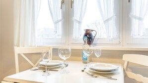A dining table with four wine glasses, a bottle, and a pitcher, set against a window with sheer curtains. - Uaster Reeg III - Studio - Sehr Gepflegte und Geschmackvoll Eingerichtete Ferienwohnungen in (Sylt / OT Archsum)