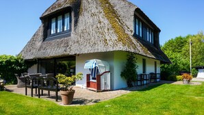 A thatched-roof house with a porch, outdoor seating, and a potted plant. - Uaster Reeg III - Studio - Sehr Gepflegte und Geschmackvoll Eingerichtete Ferienwohnungen in (Sylt / OT Archsum)