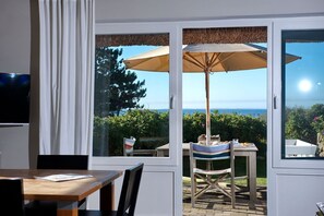 Una stanza con un tavolo e sedie in legno, un'ampia finestra vista mare e una ventola a soffitto.