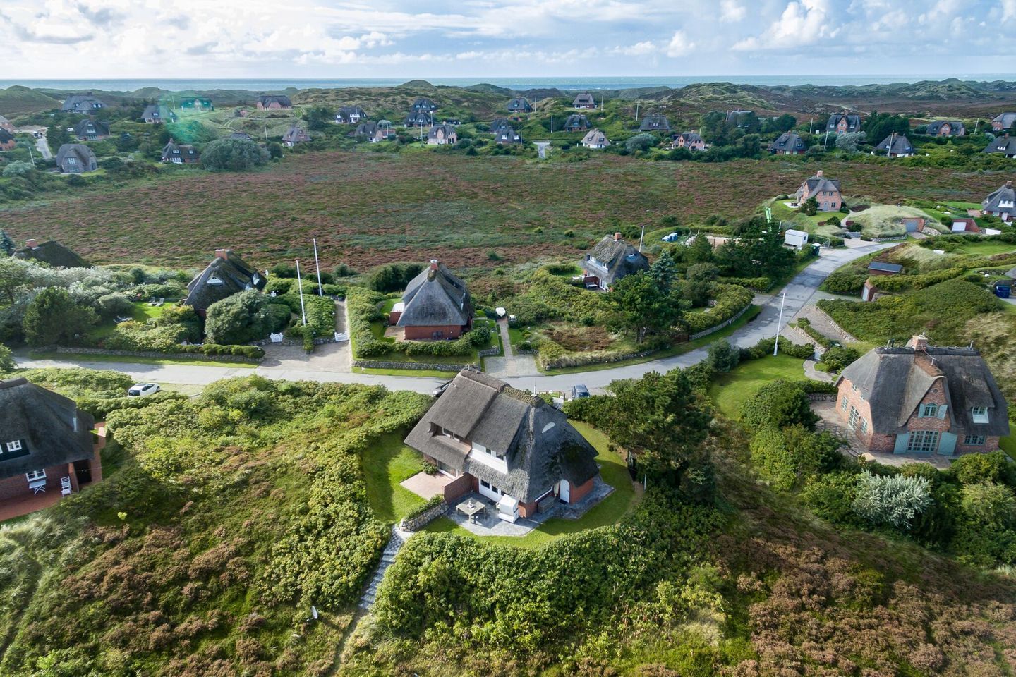 An aerial view of a rural village with traditional houses, winding roads, and a mix of open fields and hedgerows.