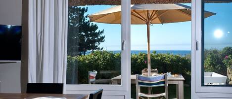 Una habitación con una mesa y sillas de madera, un ventanal con vista al mar y un ventilador de techo.