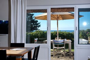 Una habitación con una mesa y sillas de madera, un ventanal con vista al mar y un ventilador de techo.