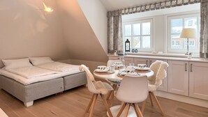 A cozy loft bedroom with a bed, a dining area with chairs and a table, and a window with curtains.