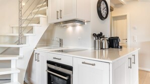 A modern kitchen with white cabinetry, a stainless steel oven, a double sink, and a coffee maker on the countertop.