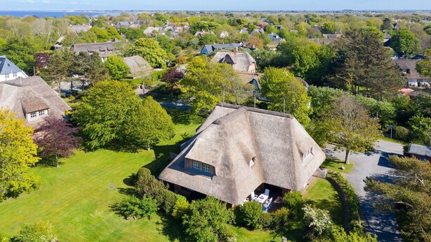 A rural village with traditional thatched-roof houses surrounded by greenery and a clear view of the sea.