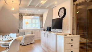 A modern kitchen with white cabinetry, a flat-screen TV, and a dining area with a white chair and table.