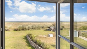 A view from a room with large windows overlooking a grassy field with a small structure and a stone wall.