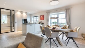 A modern kitchen with white cabinets, a dining area with a round table, and a large window with curtains.